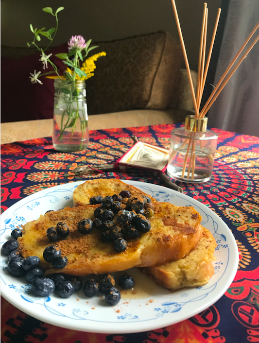 plate of French toast with blueberries on a tablecloth with a vase of flowers in the background