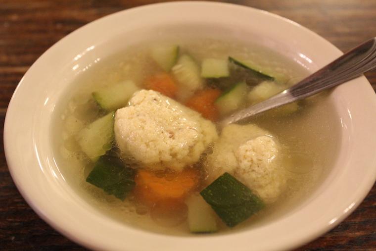 a bowl of soup with carrots, zucchini, and matzah balls