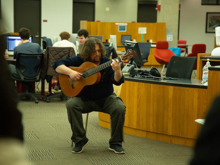A man plays guitar in the library.