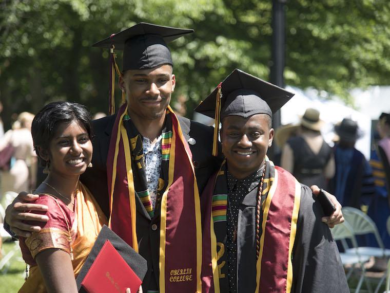three students, two in cap and gown celebrate commencement.